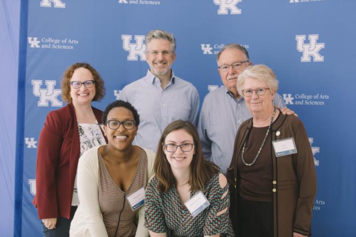 A group of six people posing in front of a blue backdrop with logos.
