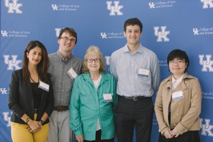 A group of five people, wearing name tags, stand together in front of a backdrop featuring the University of Kentucky College of Arts and Sciences logo.