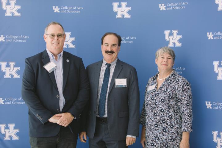 A few people stand in front of a backdrop with University of Kentucky logos.