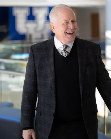 A man in a suit and tie smiles while standing in front of a blurred background with a university logo.