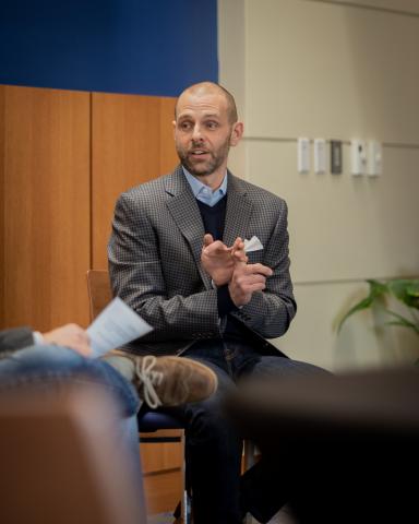 A man sits in a chair with his hands gesturing as he speaks.